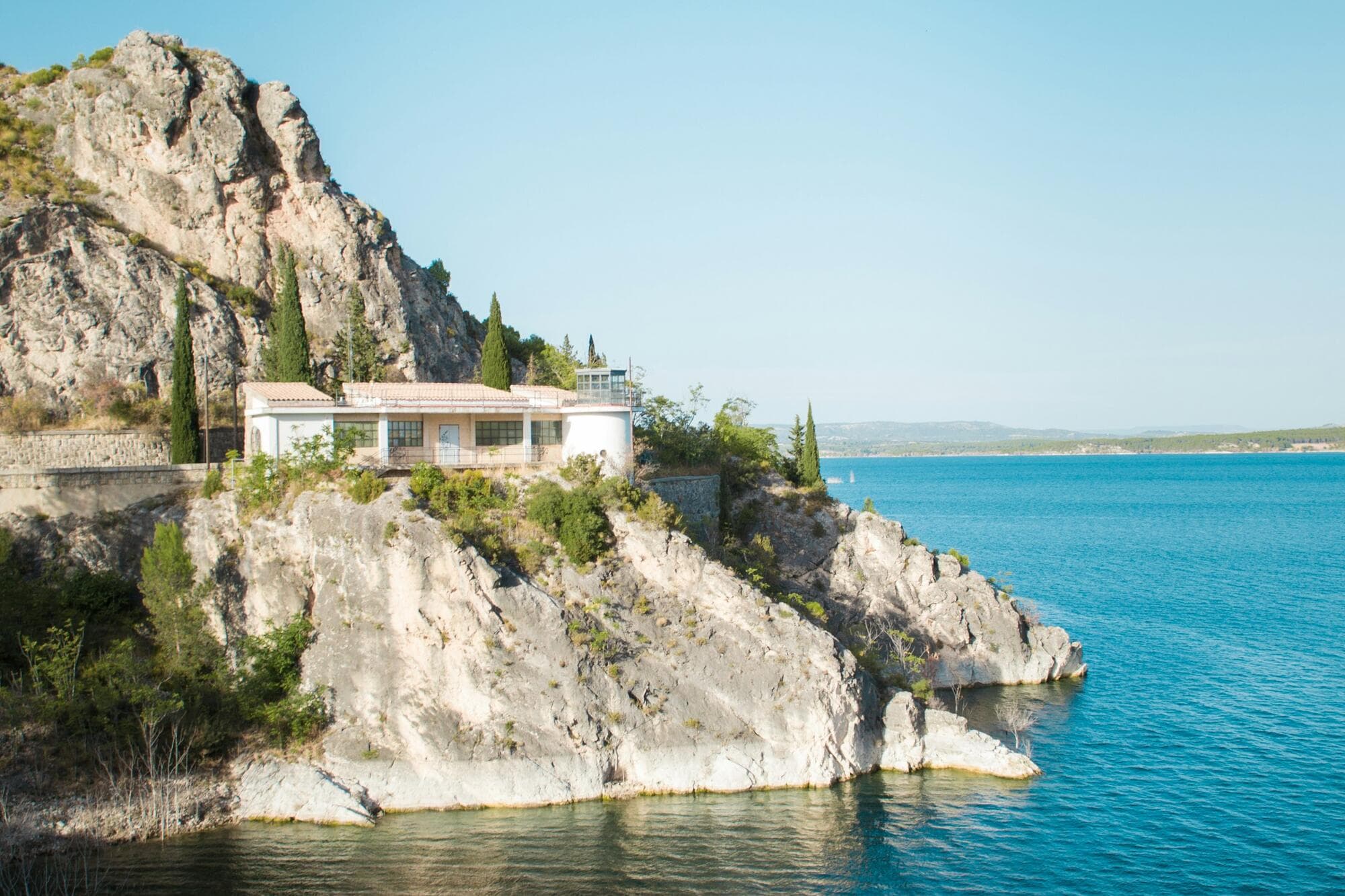 A house with big windows on the edge of still water, mountains behind