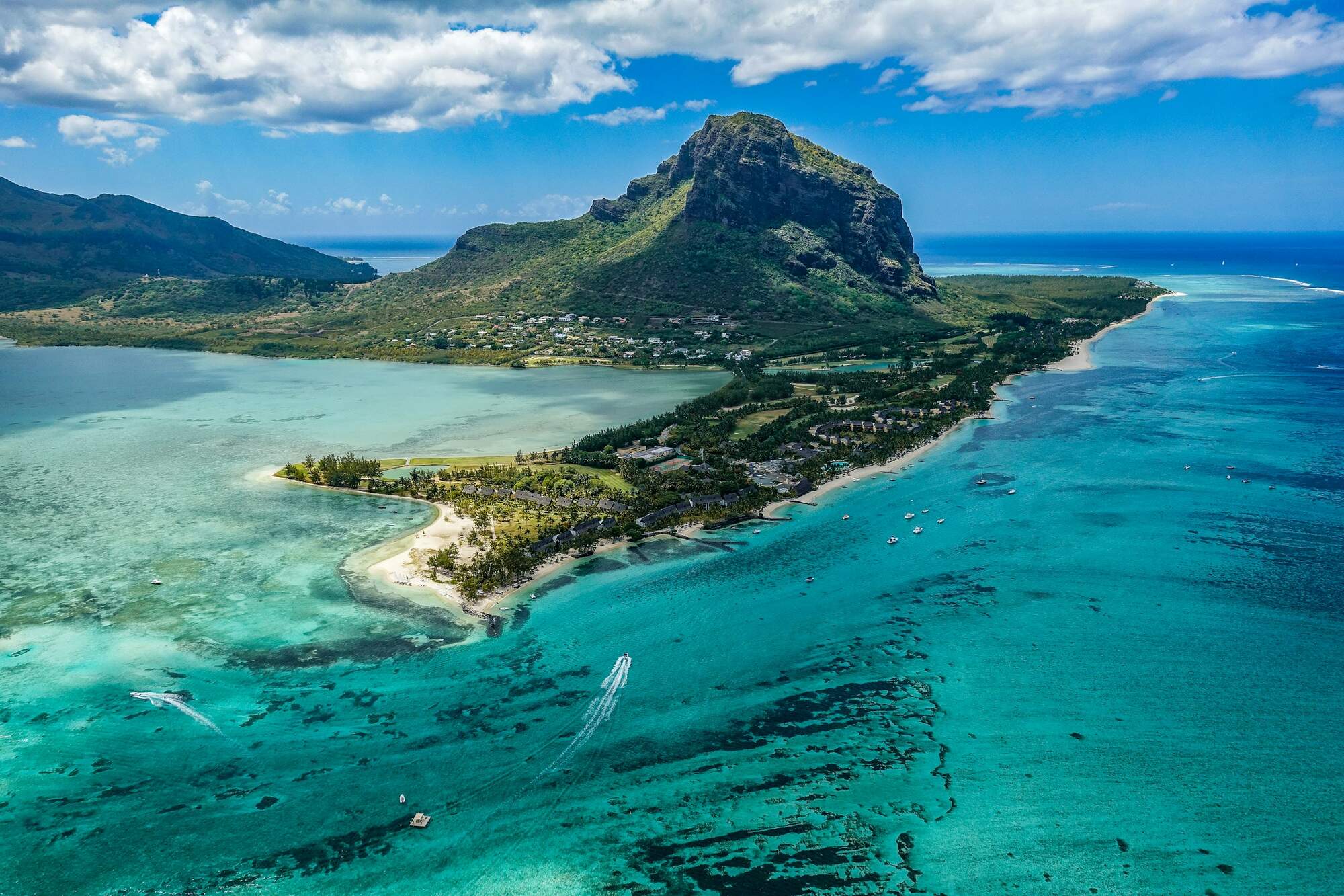 Aerial view of a beach and turquoise lagoon in Mauritius, with a mountain behind