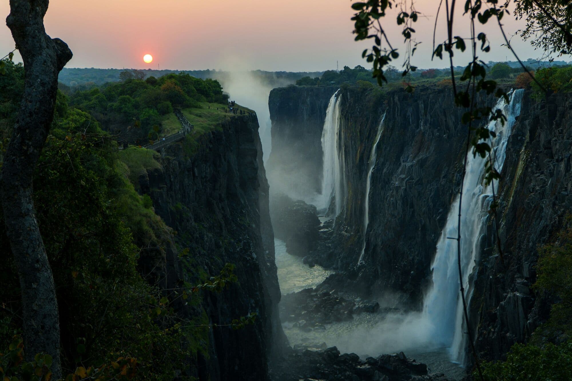 Victoria Falls at sunrise, mist rising above green trees, Zimbabwe